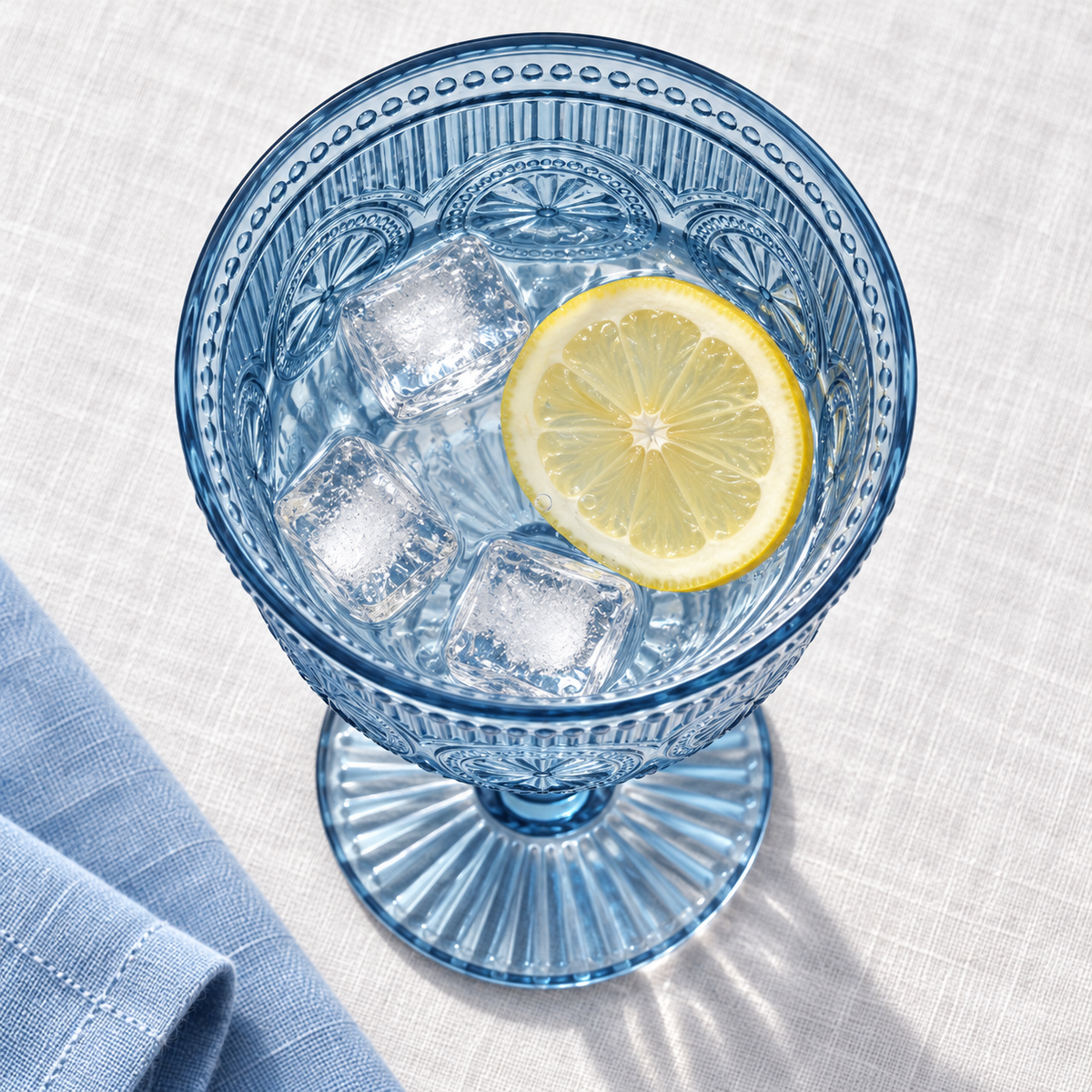 Overhead view into a smoky blue plastic goblet with cold lemon water and ice