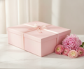 Blush-pink luxury gift box with gold-edged ribbon bow styled with pink peonies