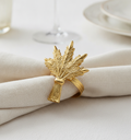 Close-up of a golden wheat-motif napkin ring on a cream napkin