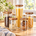 Five clear glass canisters with acacia wood lids on a bright counter