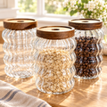 Three clear glass storage jars with wood lids on a bright cream tabletop