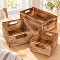 Three rustic brown wood storage crates with cutout handles in a bright room