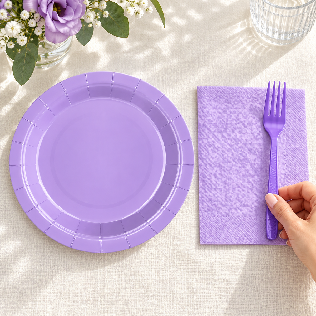 Hand arranging a purple fork beside a lavender napkin and plate; representative components from the 100-piece set for 25 guests. Background props not included.