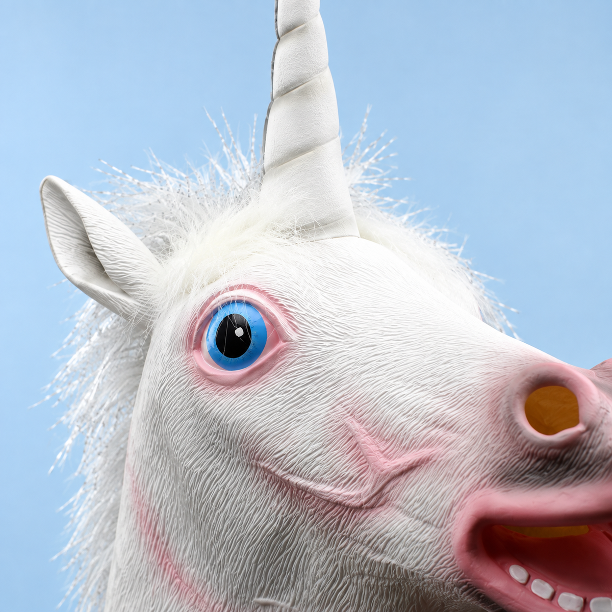Close view of the unicorn mask's horn base, ear, white mane and blue eye.