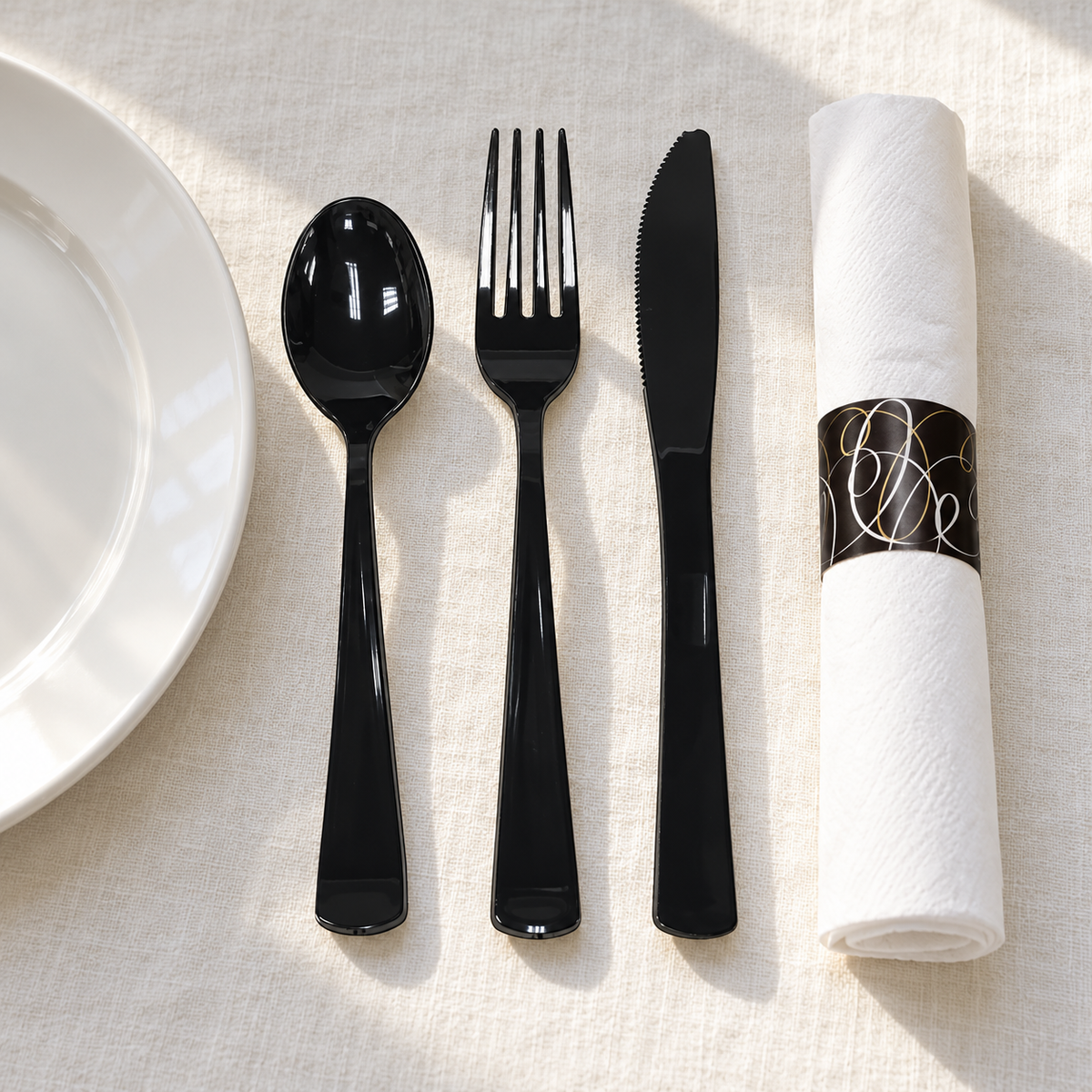 Black cutlery and a banded white napkin beside a white plate. Plate and styling props not included.