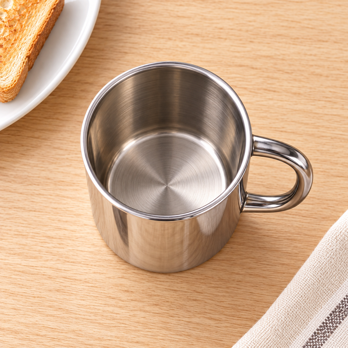 High-angle view into one empty 400 ml stainless-steel cup; breakfast accessories are styling props.