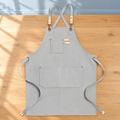Light grey canvas work apron with straps and front pockets; tools and styling accessories are not included.