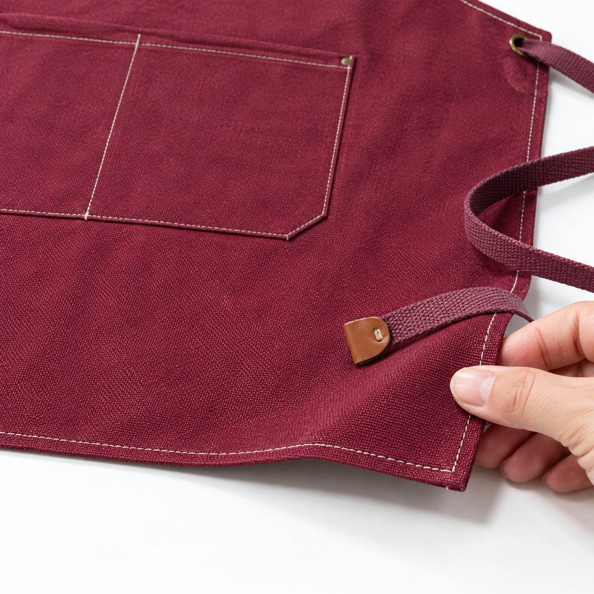 Red canvas apron lower hem, stitching and strap-end detail.