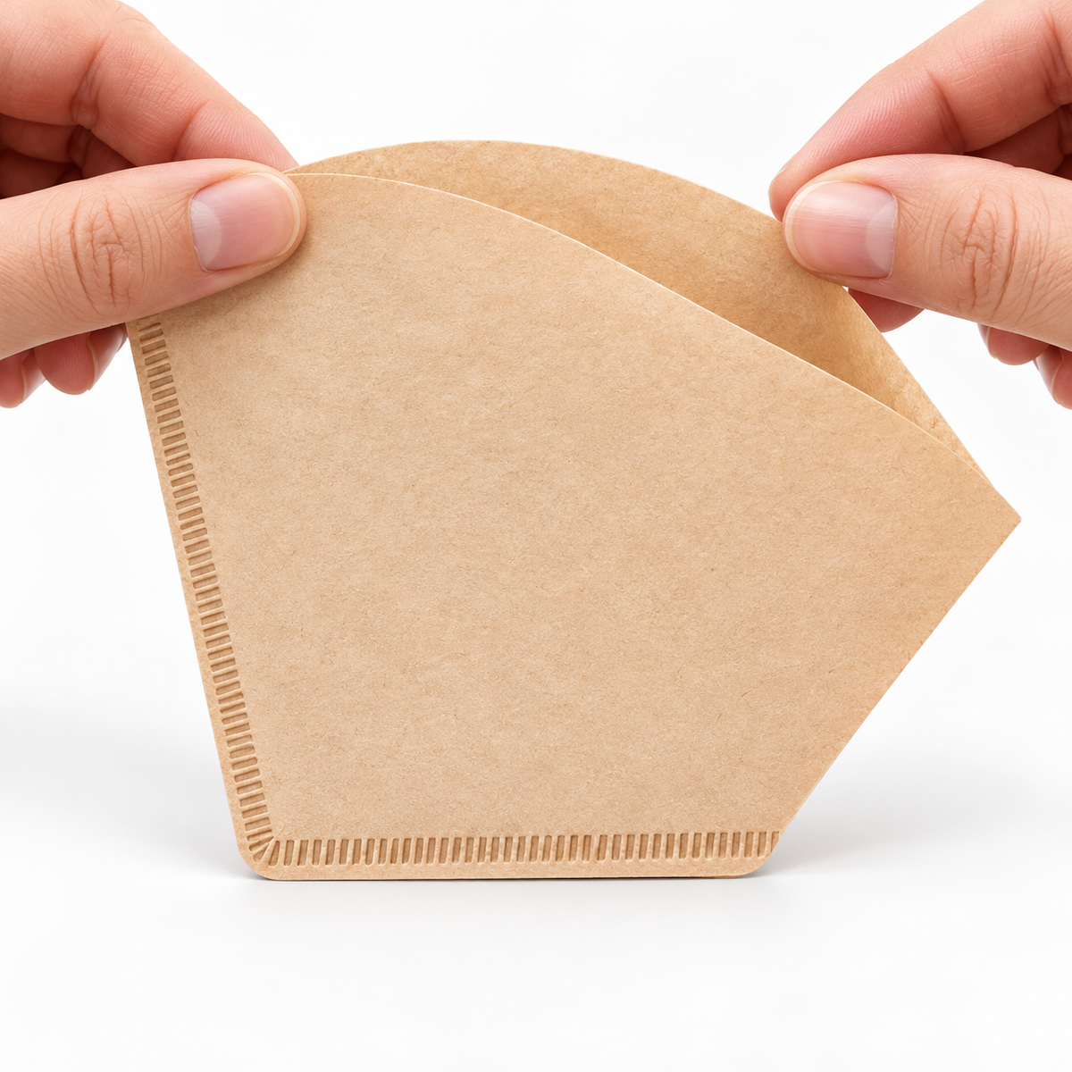 Hands opening one fan-shaped brown paper coffee filter before brewing.