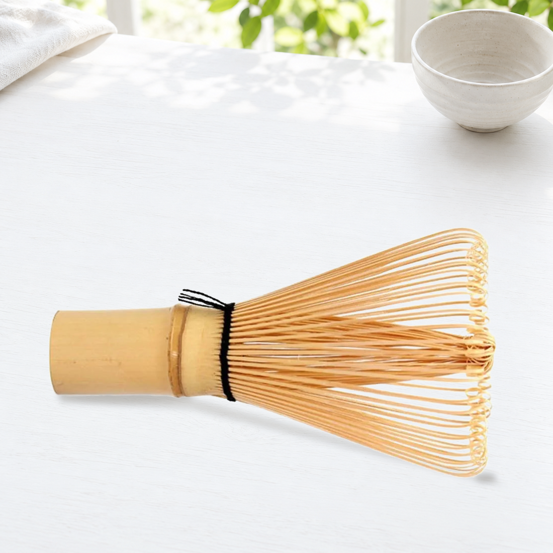 Bamboo whisk on a bright tea-preparation surface; bowl and styling accessories are not included.