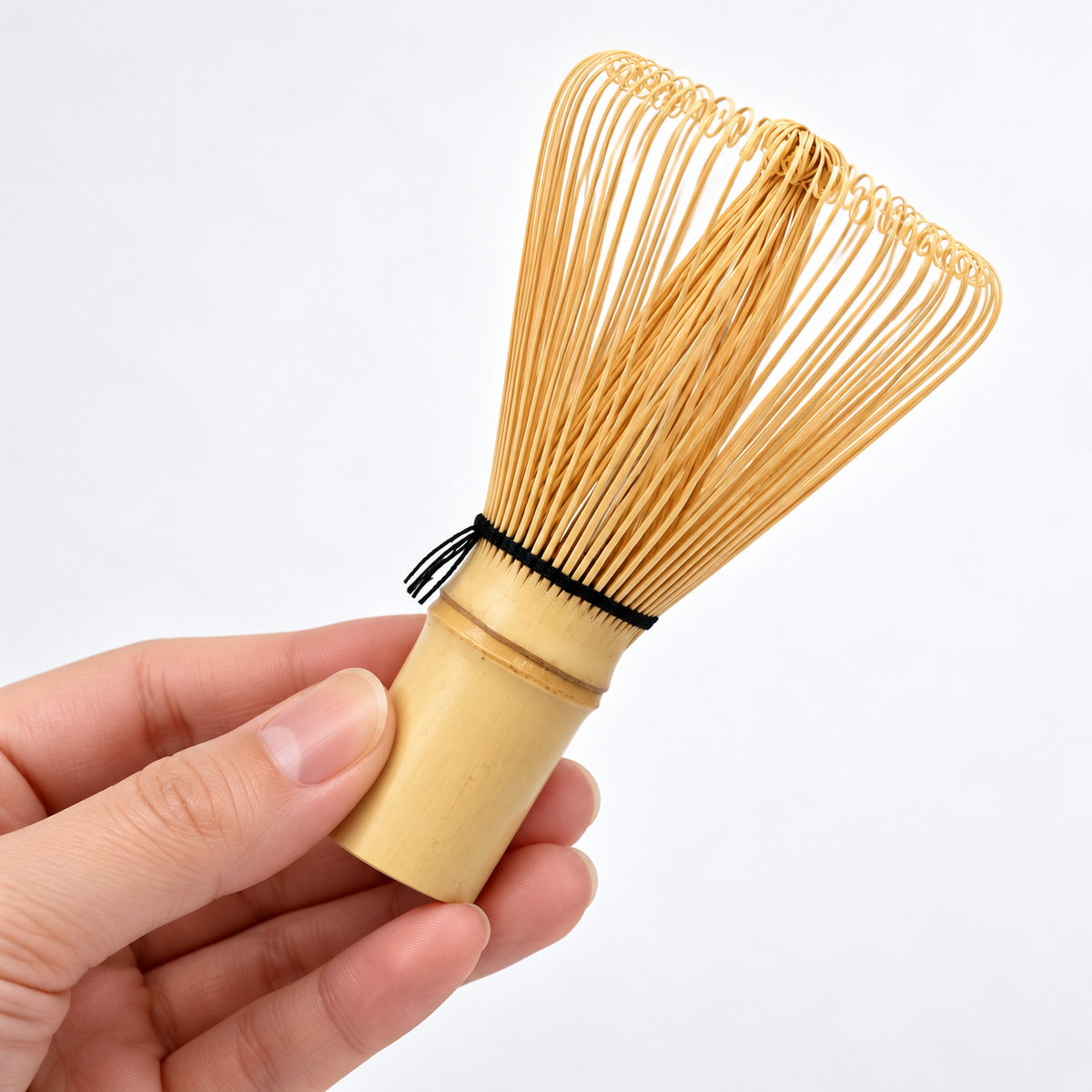 Full bamboo matcha whisk held by the handle in an adult hand.