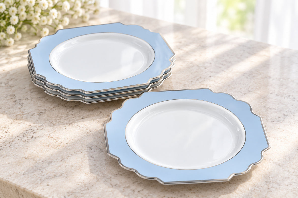 White and pale-blue ornamental appetizer plates with silver trim, shown as a short stack and a loose face-up plate beside a window. Representative selection from the pack; styling props not included.