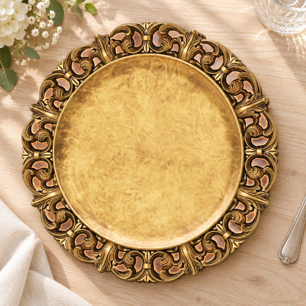 An empty antique gold charger viewed from above on pale wood, showing its mottled center and ornate embossed rim. Styling props not included.