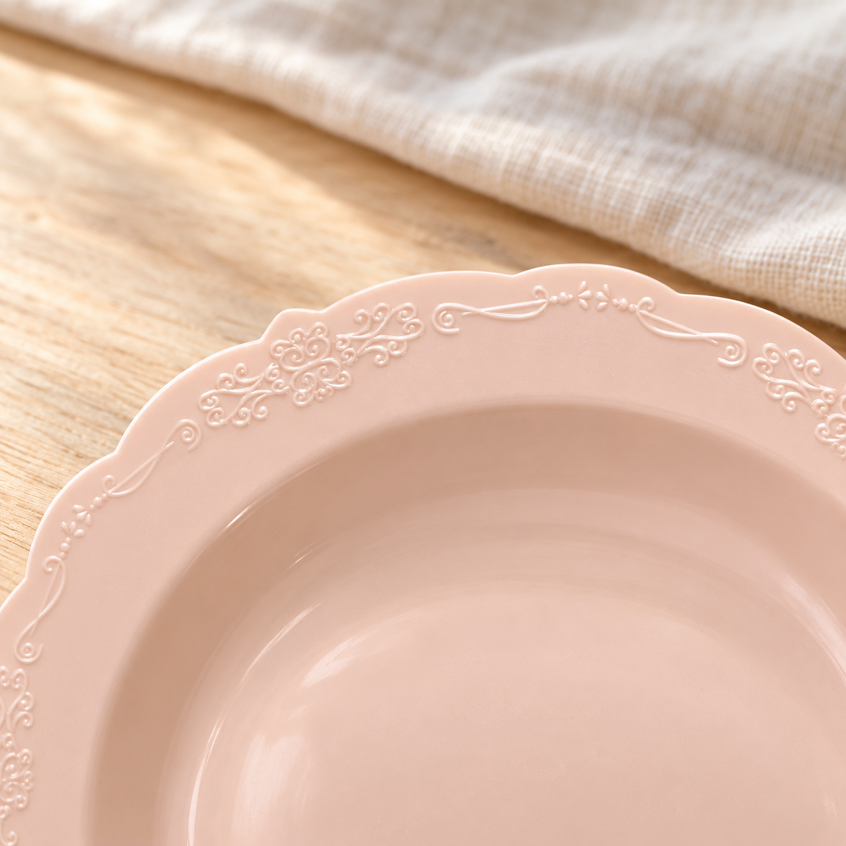 Close view of the delicate embossed scroll pattern and scalloped edge of a blush soup bowl.