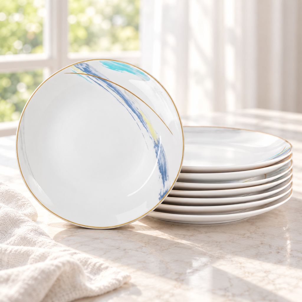 Gilded Edge ceramic plates stacked beside a single upright plate in bright window light. Linen and table are styling props. Representative arrangement from the set.