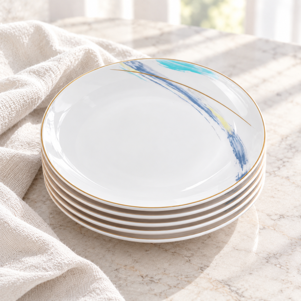 Stacked Gilded Edge ceramic plates showing shallow white edges and the decorated upper face in daylight. Linen is a styling prop. Representative arrangement from the set.