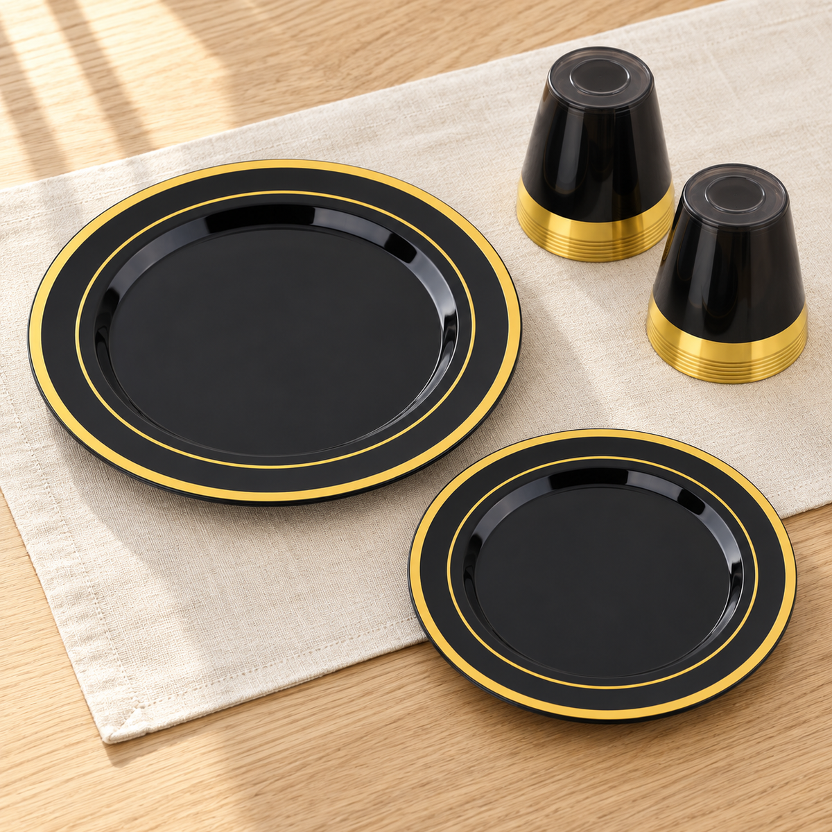 Large and small black plates with two gold rings beside inverted dark gold-rim cup stacks. Representative arrangement; styling props not included.