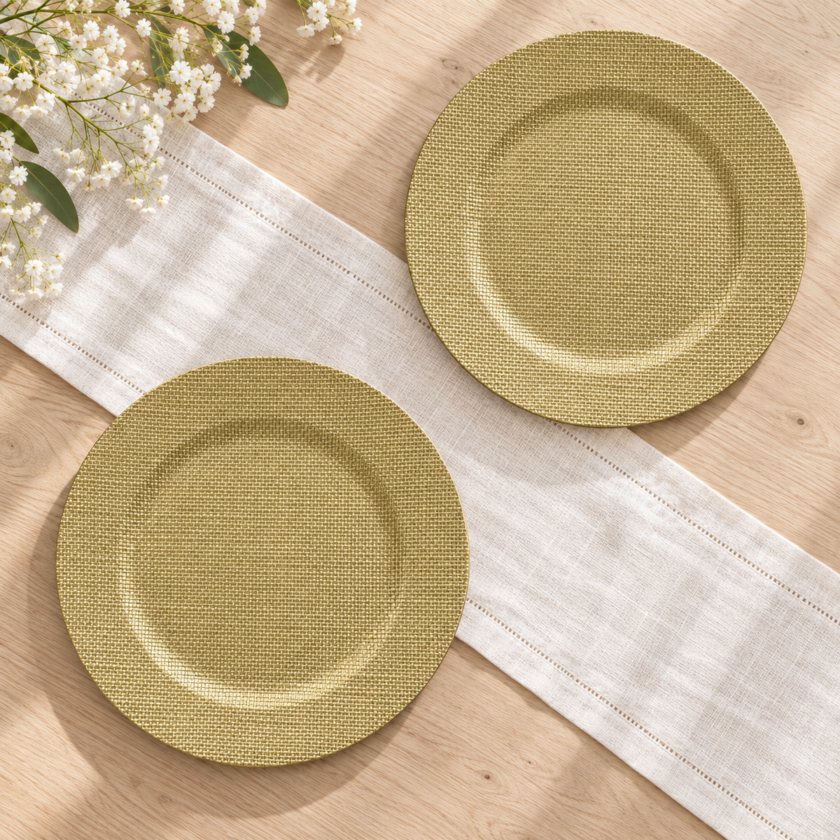 Overhead view of empty burlap-textured round chargers on a pale wood table with an ivory linen runner. Styling props not included.