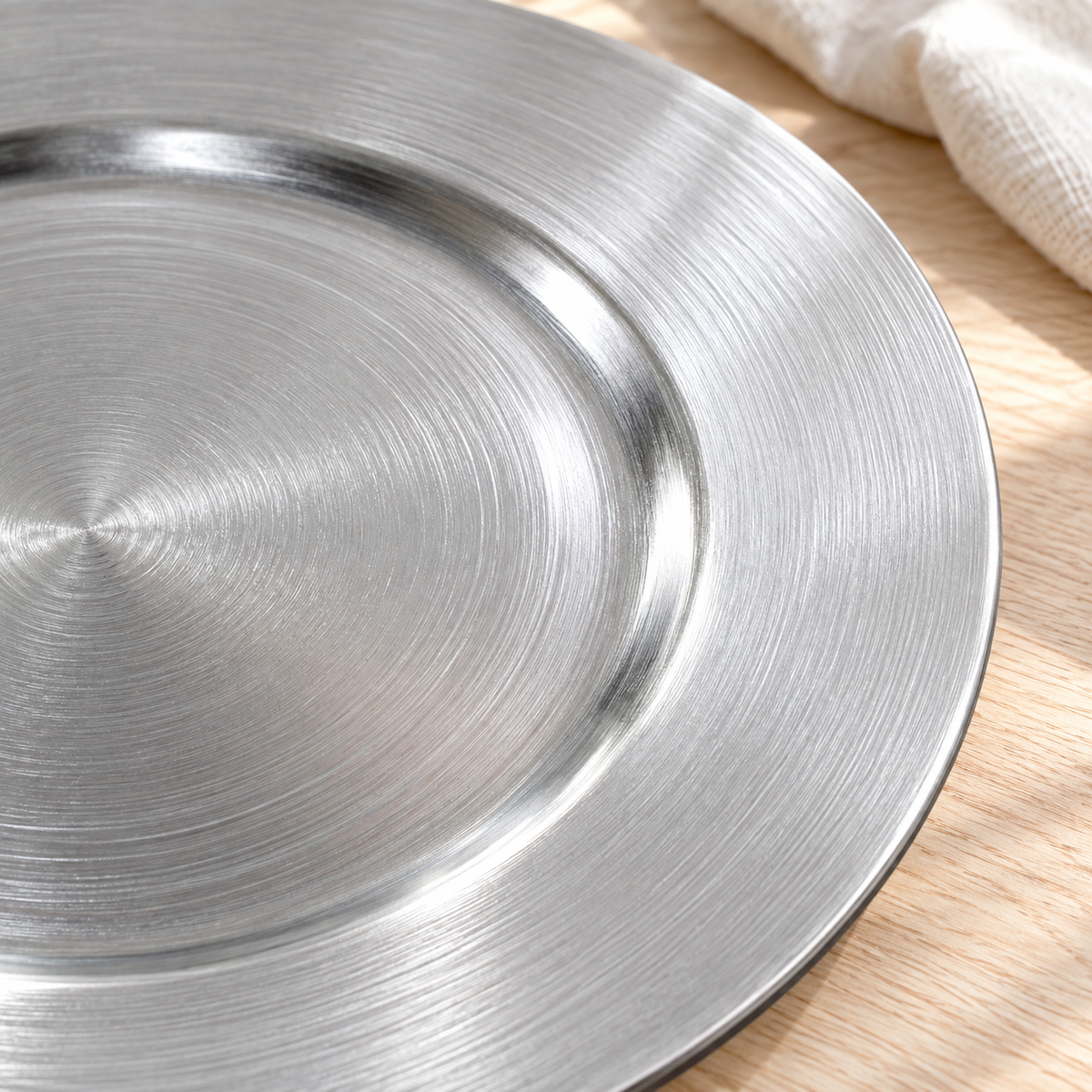 Close detail of the fine concentric brushed finish and broad rim of a metallic silver decorative charger.
