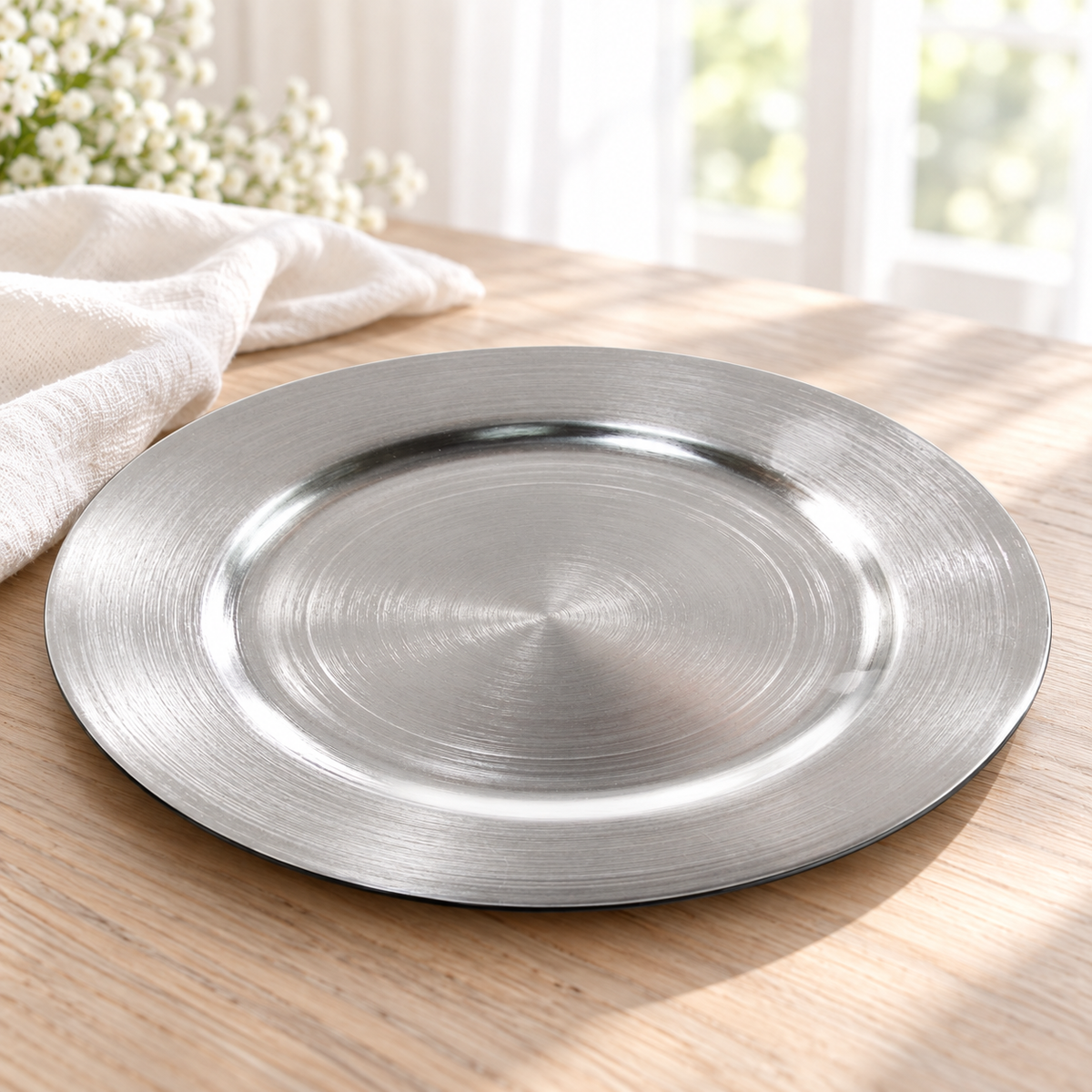 Oblique view of an empty metallic silver decorative charger showing its shallow rim and thin outer edge.
