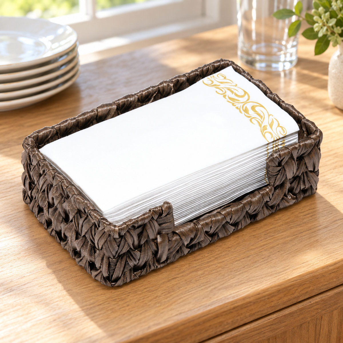 Bark Brown plastic-wicker tray holding white and gold guest towels on a wood buffet surface, with dining props in the background. Guest towels and styling props not included.