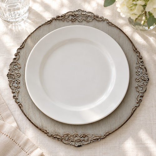 Close single-setting underplate showing antique grey decorative charger with distressed finish and ornate scroll rim. White dinner plates and styling props are not included.