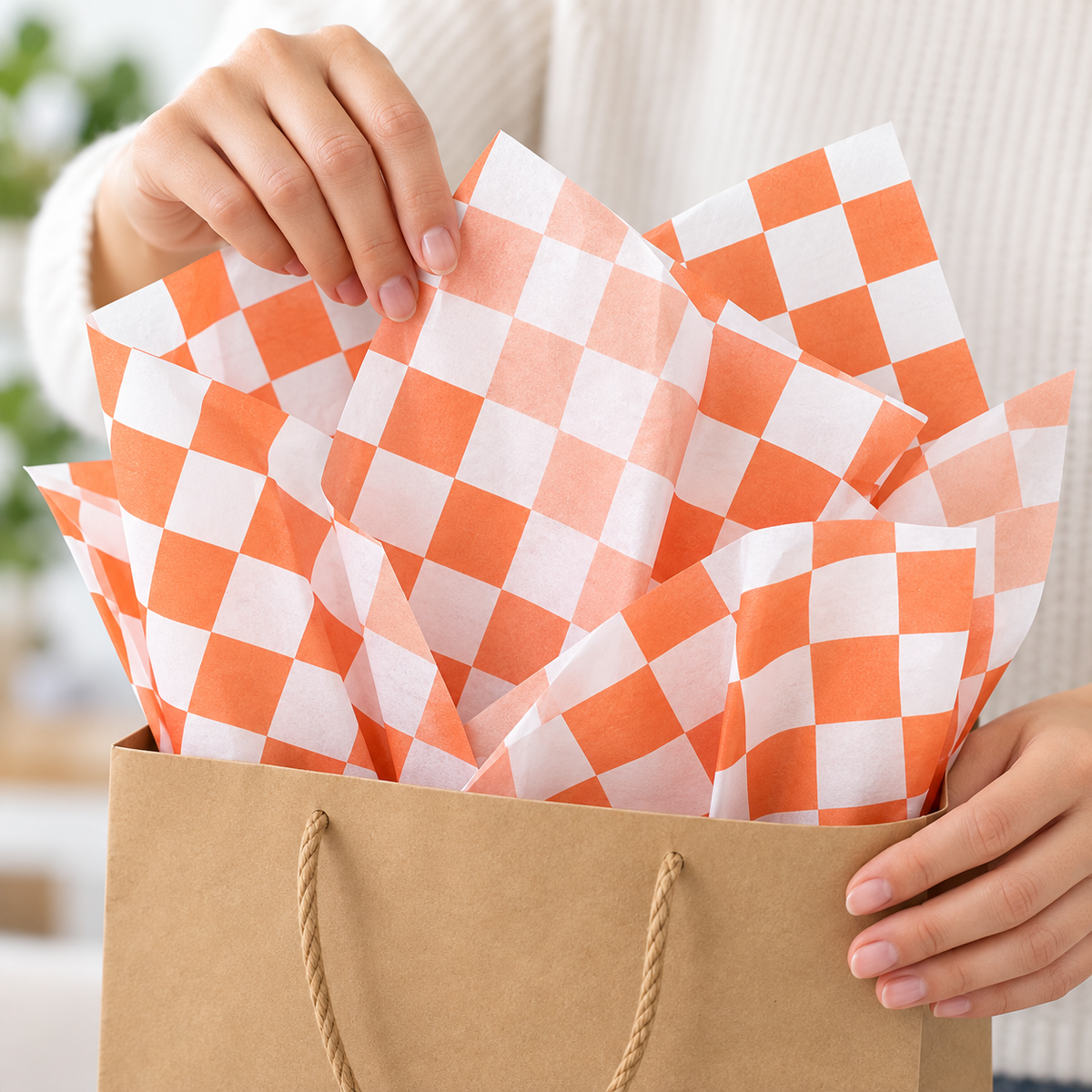 Orange and white check tissue paper, hand photograph, SKU B0DCBSMWY4. Representative sheets from 100-sheet pack; styling not included.
