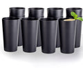Twelve matte black plastic tumblers arranged on a white background, with a lemon and mint drink in one cup. Drink and garnish not included.