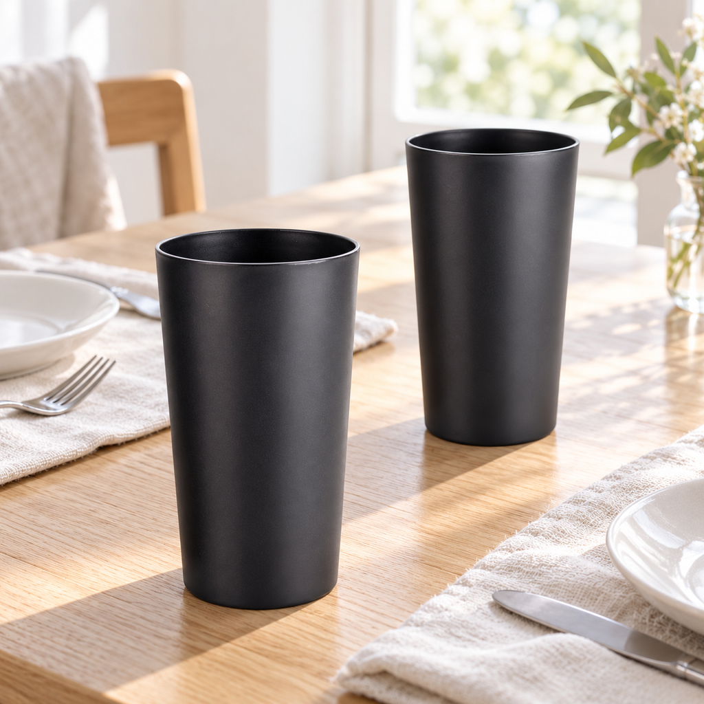Two matte black tumblers on a sunlit wood table with linen place settings. Scene props not included.