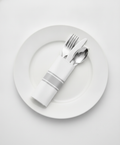 Pre-rolled silver plastic cutlery wrapped in a white napkin with a silver double-stripe band, on a white plate