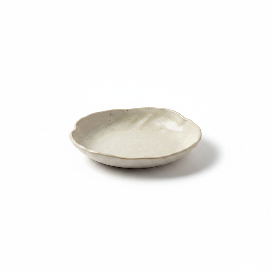 Cream handmade ceramic irregular tasting plate with wavy rim on a white background