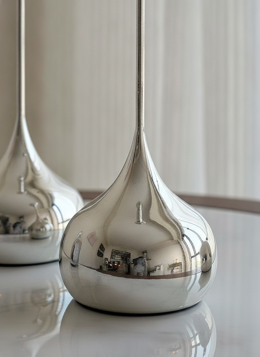 Detail of the rounded mirror-silver teardrop base reflecting warm candlelight