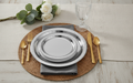Smooth silver paper party plates place setting on a rattan placemat with gold flatware and white roses