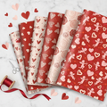 Overhead flat-lay of Valentine heart wrapping paper sheets with ribbon and scissors
