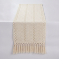 Ivory macrame cotton table runner with openwork weave and hand-knotted tassels, draped on a soft-white studio surface