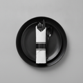 Black plastic cutlery set pre-rolled in a white napkin with black band on a matte black plate