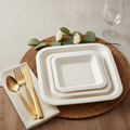 White molded sugarcane bagasse square disposable plates styled on a woven placemat with gold flatware