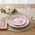 Pink floral disposable plastic party plates styled in a place setting with gold flatware, woven placemat and white roses