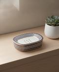 Empty striped ceramic soap dish on a light wood bathroom shelf with a plant