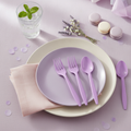 Two purple plastic forks and two purple plastic spoons at a pastel party place setting; tableware is styling only.