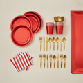 Overhead flat-lay of shiny red paper plates, cups, gold cutlery and striped napkins