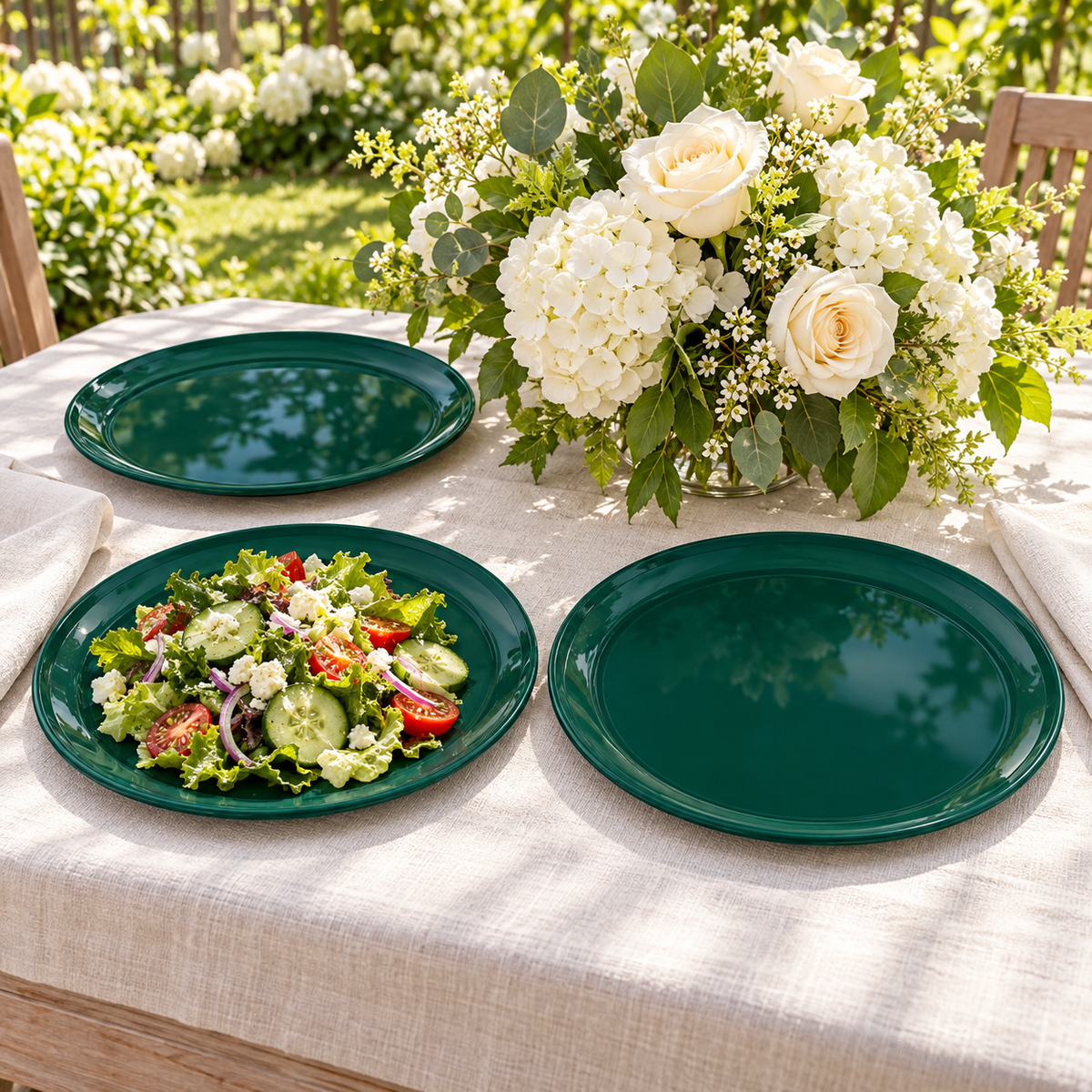 Dark green plastic dinner plates with a fresh salad on a bright garden table with cream flowers. Food and styling props not included.