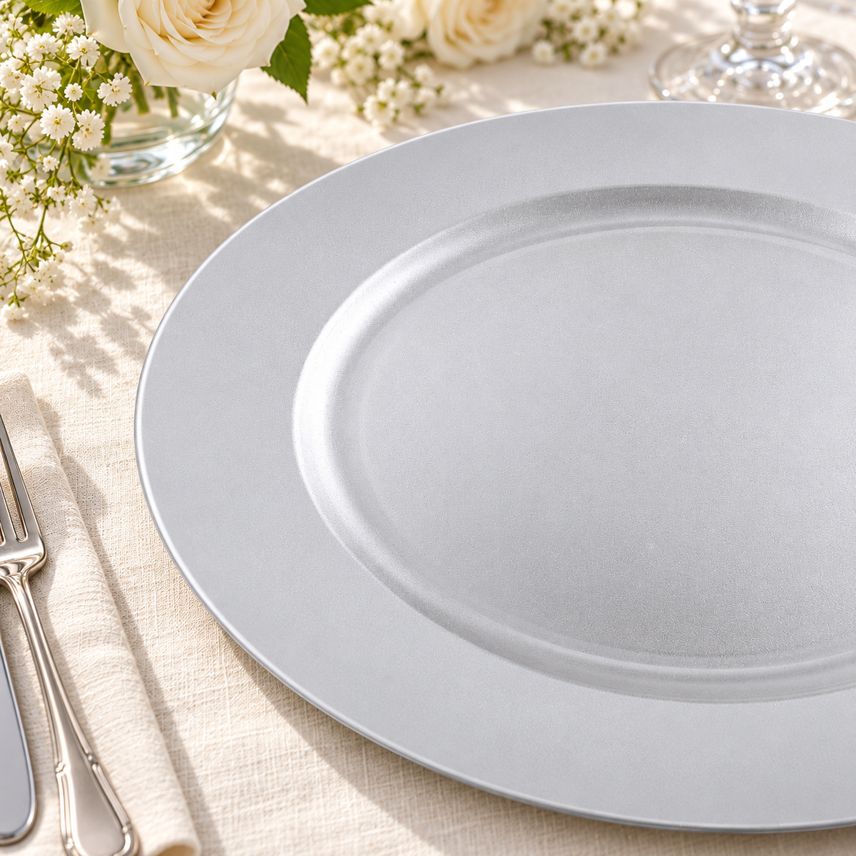 Close view of the silver white charger’s plain rim, recessed center and fine irregular satin finish on ivory linen. Representative arrangement; food and styling props not included.