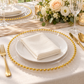 Clear charger with a single gold beaded rim beneath a separate white plate and folded ivory napkin on a linen celebration table. Representative arrangement; food and styling props not included.