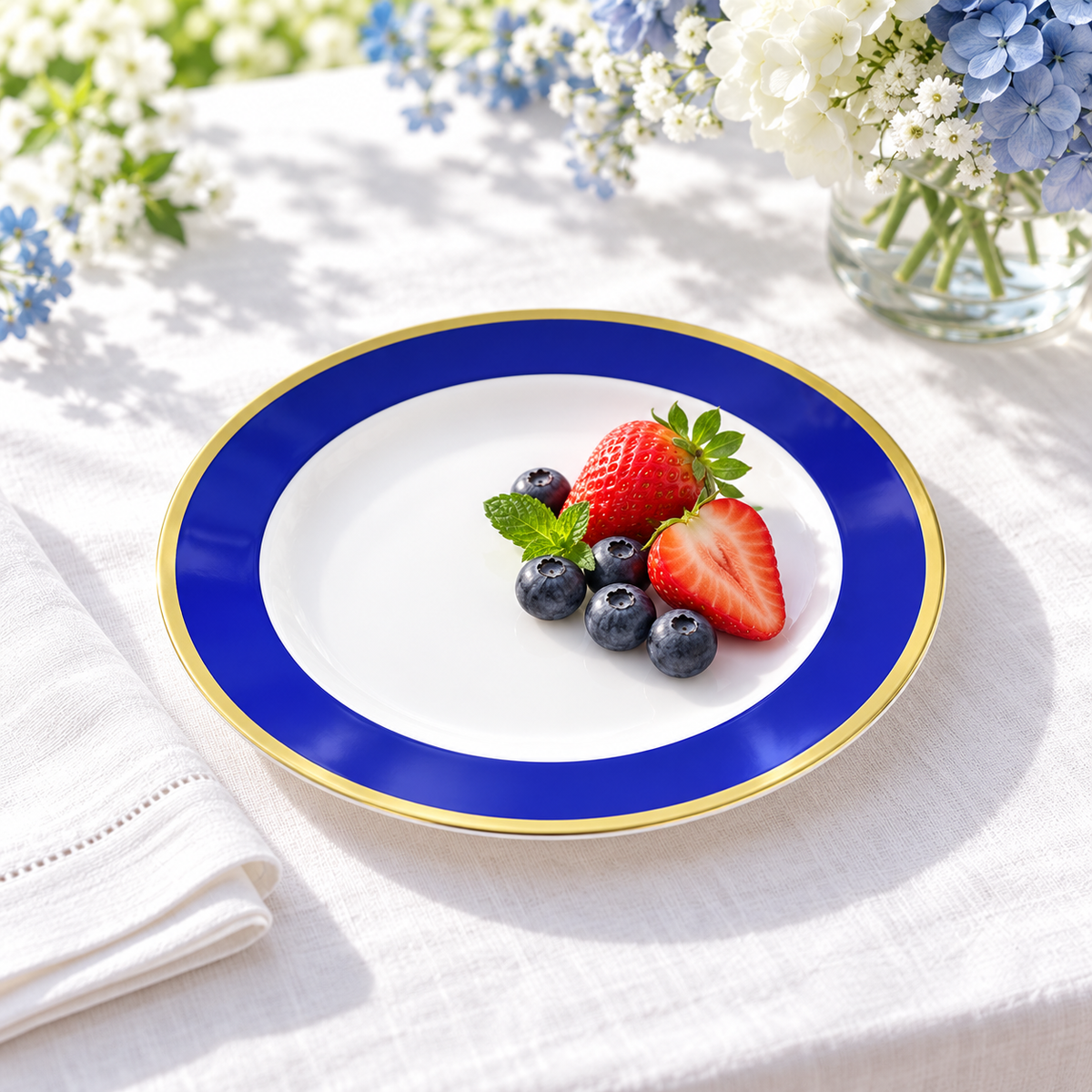 Small blue and gold plate with strawberries and blueberries on white linen beside blue and white flowers. Representative arrangement; food and styling props not included.