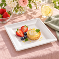 Small white square plate holding a mini tart and berries on blush linen beside flowers and lemonade. Representative arrangement; food and styling props not included.