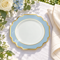 One white, dusty blue and gold small plate on ivory linen beside white roses, pale blue hydrangeas and a folded napkin. Representative arrangement; food and styling props not included.