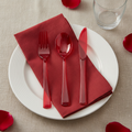 Festive red plastic cutlery on a white plate with a red napkin party place setting