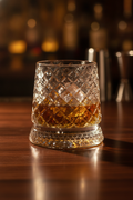 Crystal whiskey tumbler holding amber whiskey with a clear ice sphere on a walnut bar