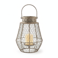 Intreccio woven wire candle lantern with antique iron patina and arched handle, holding a glowing pillar candle